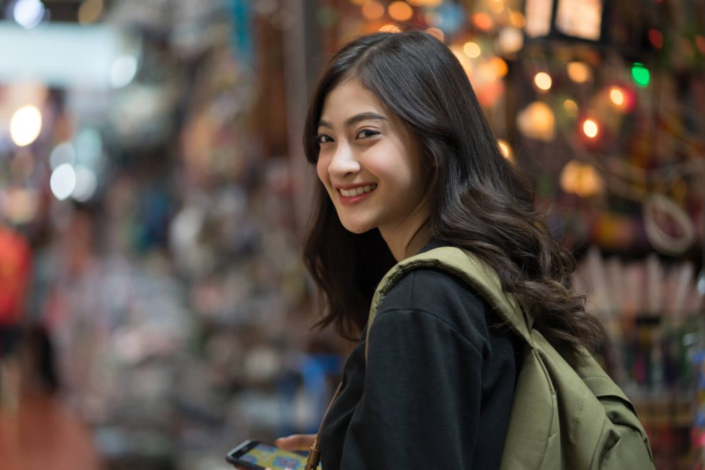 A young female traveler smiling while exploring a bustling Bangkok street market.