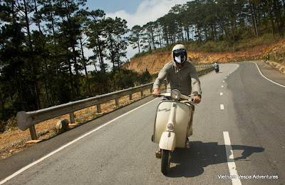 A Vespa rider wearing a helmet and sunglasses, cruising down an open mountain road in Vietnam.
