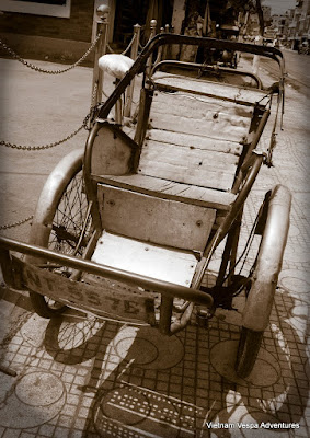 An antique rickshaw parked on a cobbled street in Vietnam, showcasing traditional transportation history.