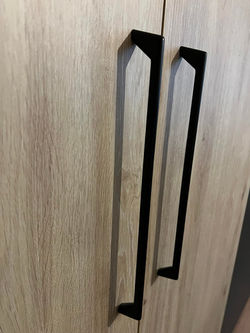 Détail de poignée noire sur porte de placard en bois clair. Une finition soignée pour un agencement 