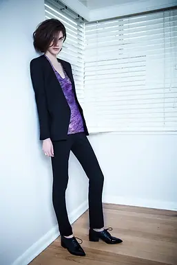 FASHION MODEL IN LIVING ROOM WEARING SILK PUPRLE PRINT TEE AND SLIM CIGARETTE PANT AND TAILORED JACKETLOWES NEODIA
