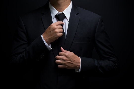 A man in a black suit, white shirt and black tie.