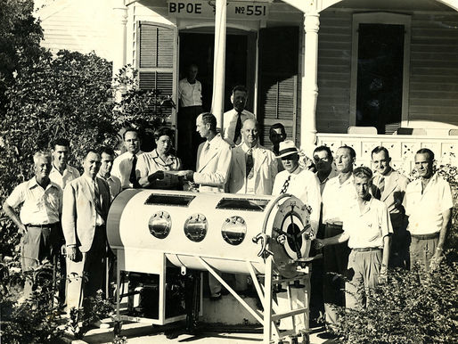 Group of men in suits gather around a cylindrical medical device outside a building labeled "BPOE No 551."