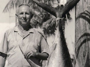 A man standing next to a large fish, hanging vertically.