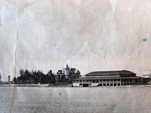 A building on a shoreline with a long porch, seen from the water.