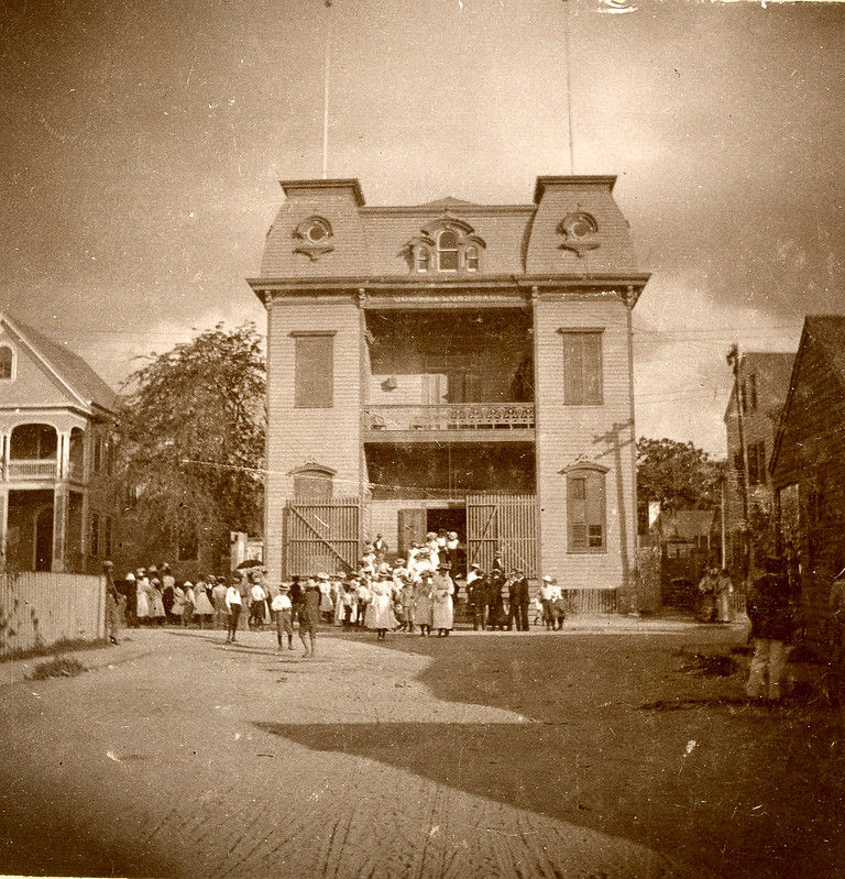 A group of people in front of a three story building with a mansard roof.