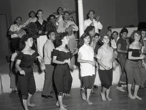 A group of people on a dance floor and musicians on a stage behind them.