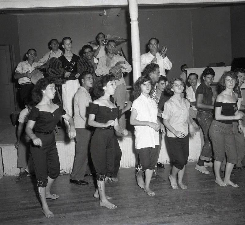 A group of people on a dance floor and musicians on a stage behind them.
