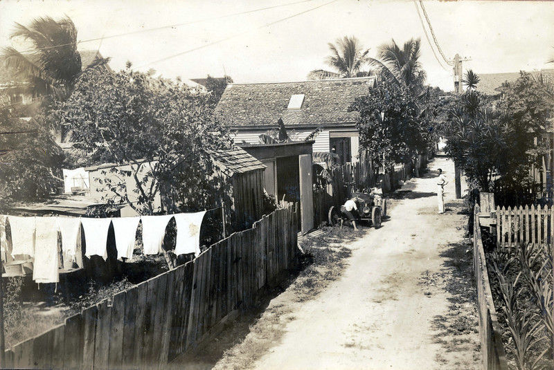 A dirty lane with houses and fences and laundry hanging on a line at the sides.