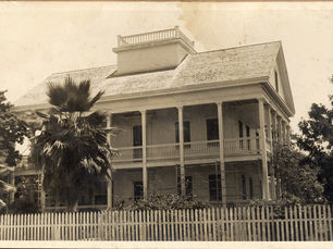 a wooden house with porches on the first and second floors and a widow's walk on the roof.