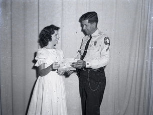 A man in a police uniform hands a piece of paper to a girl.
