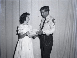 A man in a police uniform hands a piece of paper to a girl.