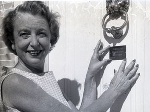 A woman in front of a door with a plaque and door knocker