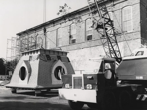 a clock tower and crane on the ground next to a brick building.