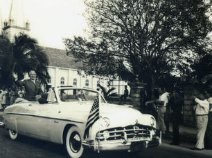 a man waves to people rfom the back of a convertible with an American flag on the front