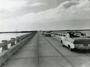 A line of 1950s style cars crossing a bridge