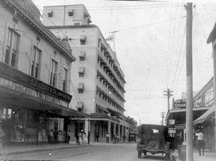 A street with large buildings and an early 20th century car