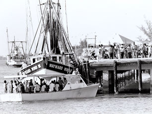 A small commercial fishing boat with a lot of people on it appraoches a dock that has a lot of people on it.