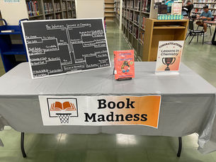 A table with brackets, a sign reading book madness and a copy of Lessons In Chemistry.