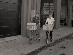 Two young men with bicycles with large baskets on a sidewalk