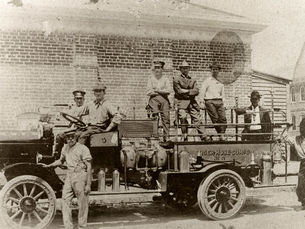 a group of men on and around an old-fashioned fire engine