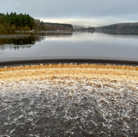 Water runs off the edge of a reservoir with a winter landscape in the background.