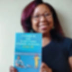 Smiling woman holds a book titled "I Turned 40 and Everything Stopped Working—Even Me" with a colorful cartoon cover, against a plain background.