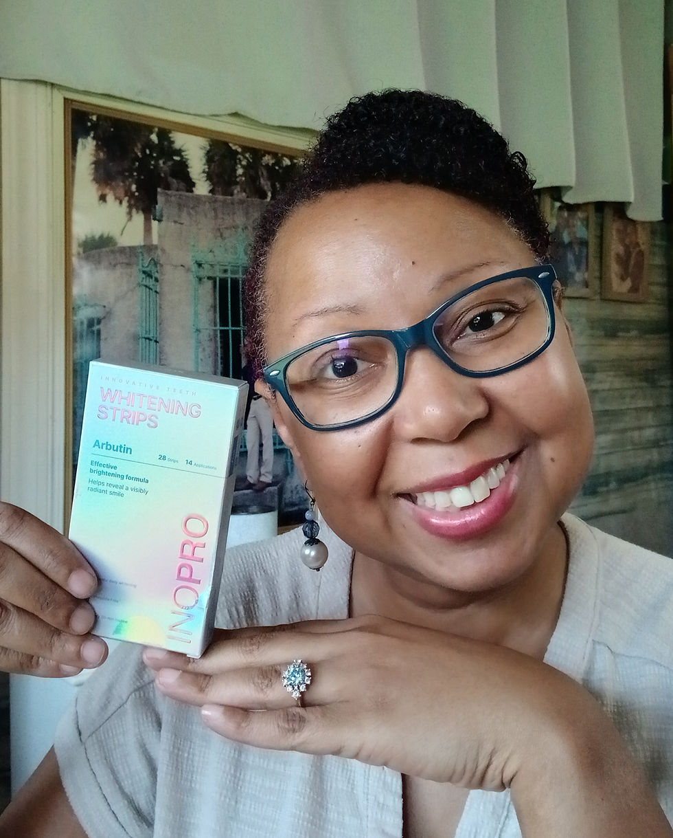 Smiling woman in glasses holds INOPRO Whitening Strips box indoors, with framed wall art behind her.