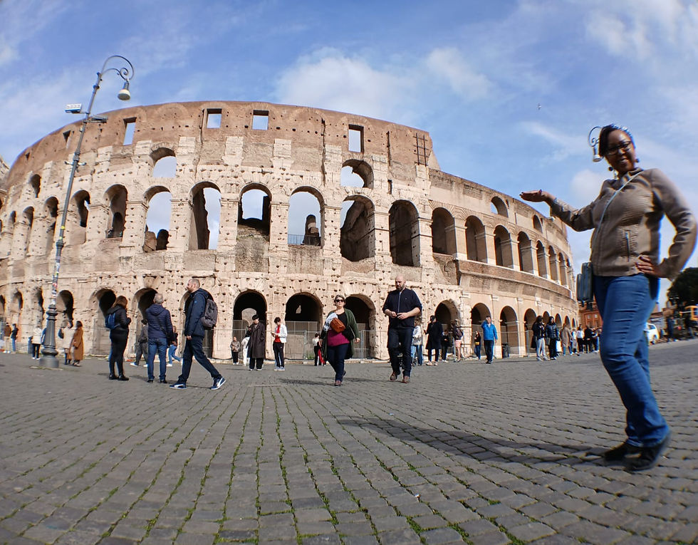A woman poses playfully in front of the Colosseum in Rome, surrounded by tourists. The sky is clear and the mood is lively.