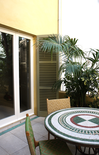 Dining area on the balcony with a mosaic table accentuated by green window shutters and planting