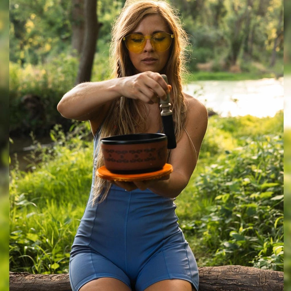 Woman meditating with singing bowl and mallet in lush nature.