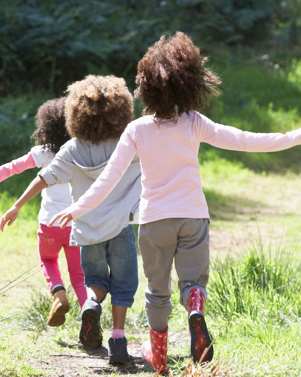 Three children joyfully run on a grassy path in a forest in an holiday playful mood.