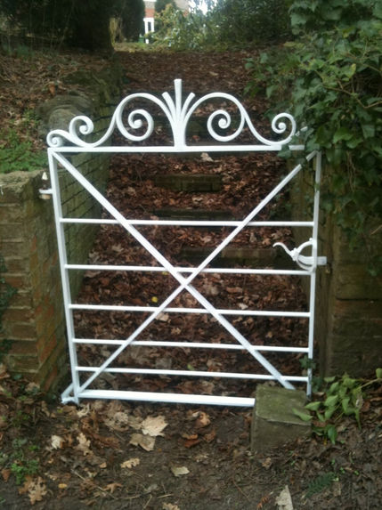 Decorative white steel gate with ornamental scrolls on top, installed at the bottom of a garden path with stone steps