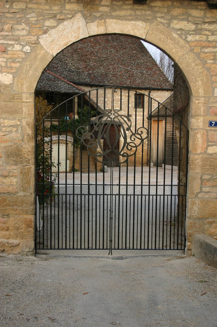 Handcrafted arched steel gate with a central ornamental crest installed in a rustic stone archway entrance.