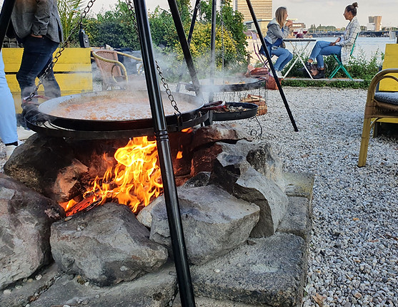 Paella préparée sur le feu à l'aide d'un BBQ suspendu.
