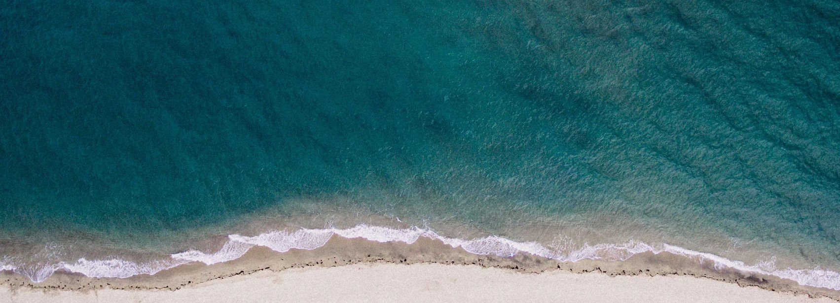Vista aérea de una playa de arena fina y mar turquesa, con olas rompiendo suavemente en la costa, playa desierta ideal para nadar y relajarse junto al mar.