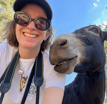 A woman with a dark donkey. They are taking a selfie together and the donkey is smiling a little.