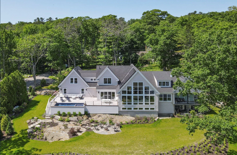 Large modern home with pool surrounded by lush green trees and landscape.