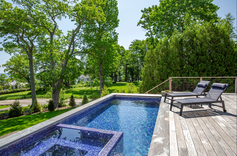 Luxury swimming pool with two chairs, surrounded by lush trees and greenery.