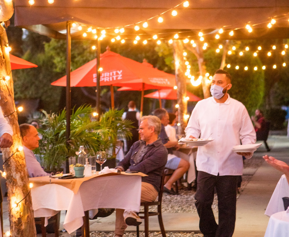 Photo of masked waiter serving food to patio diners.