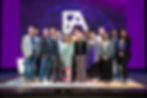 The Founders Arena team stands in front of a purple screen with a large Founders Arena logo on it