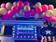 balloons along the ceiling with a captain america statue and a sign saying "Now Showing Deepdub.ai"