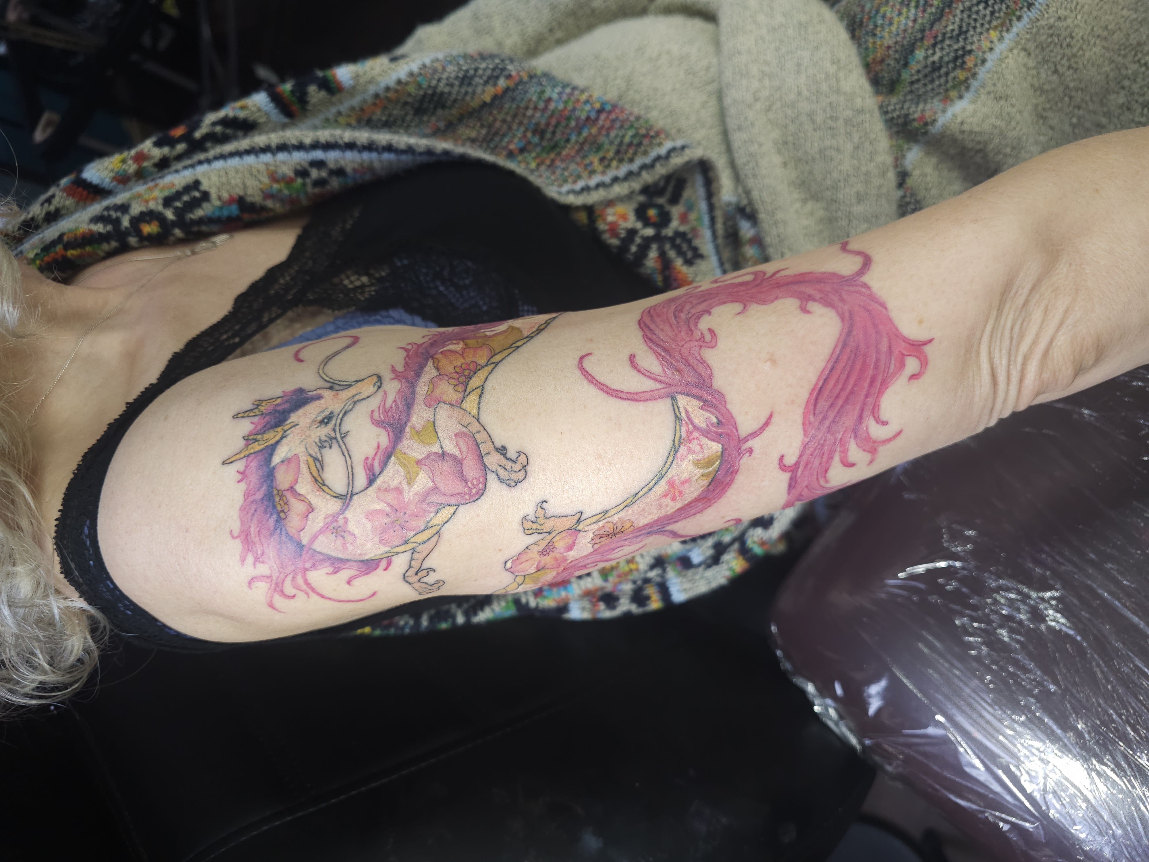 Pink dragon tattoo with flowing ornamental shapes and floral details on the upper arm.