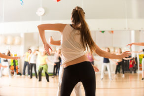 An exercise class instructor facing away from the camera in front of an exercise class in progress.
