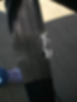 Close-up of a frayed black seat belt against a concrete ground. One blue sneaker is partially visible, suggesting wear or damage.