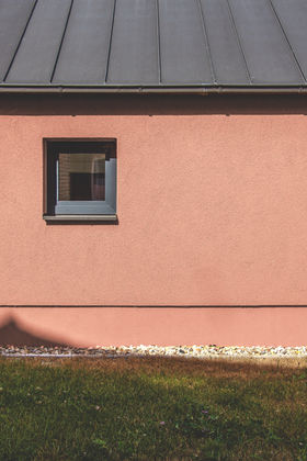 Eine rote Putzfassade mit anthrazitfarbener Metalldacheindeckung und anthrazitfarbenen Fenster