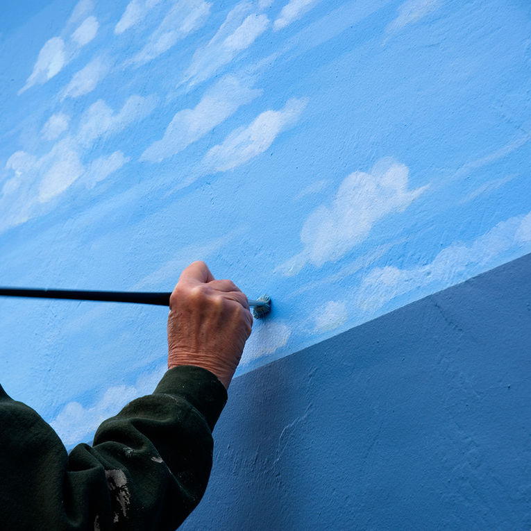 An artist holding a paint brush painting clouds