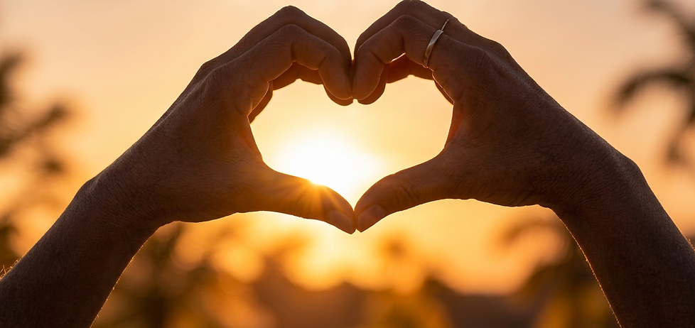 Close-up photography of hands forming a heart shape with the sun setting behind them. The warm, golden light creates a romantic and hopeful mood.