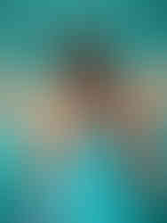 Woman in teal dress and orange blazer outfit poses in front of teal backdrop inside Durham NC photography studio