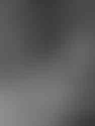 Black and white image of mother and daughter sitting side by side, holding hands and smiling at the camera in an indoor photo studio